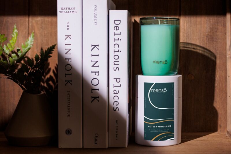 a menso candle set on a shelf with books. there is a warm, cosy "home" feeling.