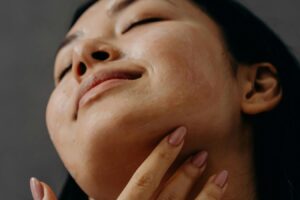 A woman gently touching her chin and neck, with a relaxed expression and glowing skin.
