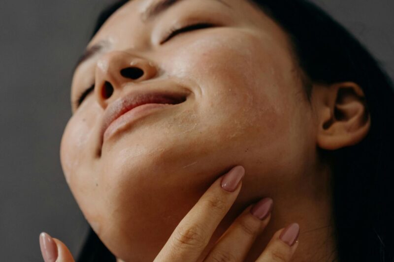 A woman gently touching her chin and neck, with a relaxed expression and glowing skin.