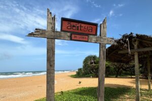 A wooden sign on the beach reads "Aditya,"