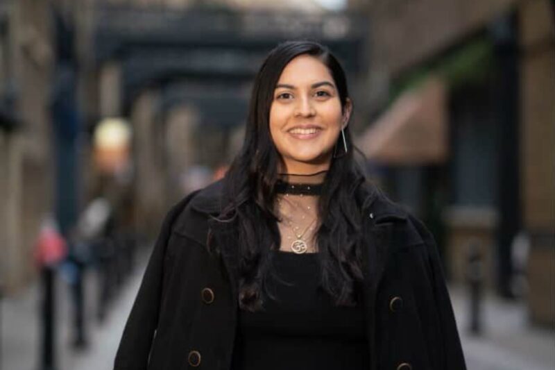 A woman in a black dress and coat stands confidently