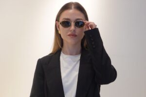 Emma, dressed in a black suit and sunglasses, stands confidently, showcasing a stylish and professional appearance.