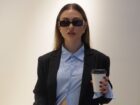 In an interview series, Emma wears a suit and sunglasses while holding a coffee cup