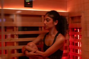 A woman enjoys the warmth of an infrared sauna, bathed in red light, promoting relaxation and wellness
