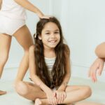 Two girls on the floor, one sitting cross-legged, both dressed in Just Peachy brand outfits, smiling and chatting