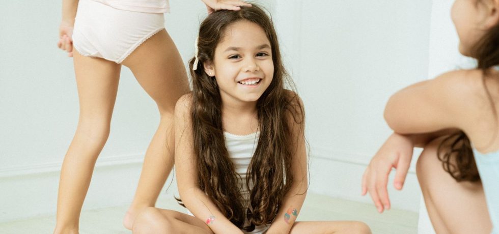 Two girls on the floor, one sitting cross-legged, both dressed in Just Peachy brand outfits, smiling and chatting