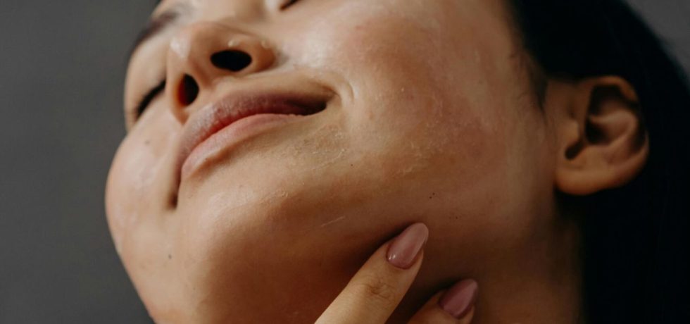 A woman gently touching her chin and neck, with a relaxed expression and glowing skin.